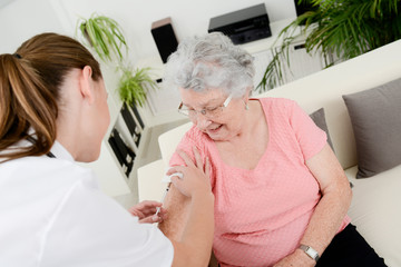 cheerful young nurse giving a vaccine injection to elderly woman at home