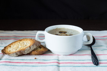 Bowl of mushroom soup with bread on wooden board. Recipe or menu background