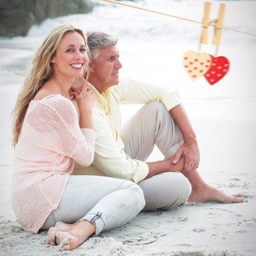 Composite image of happy couple sitting on the sand
