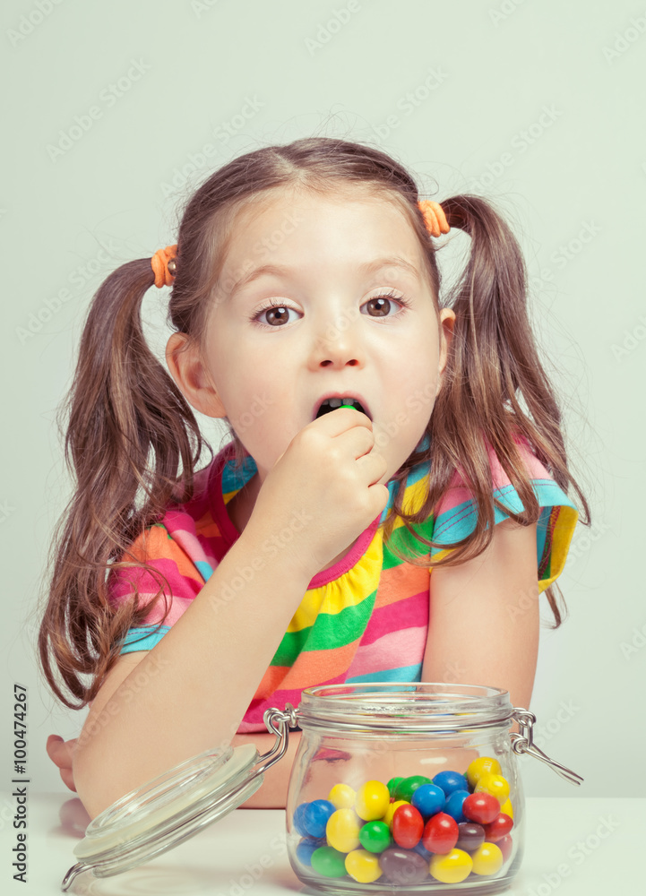 Wall mural beautiful cute little girl eating candy from candy jar