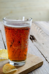 Beer into glass on wooden table with potato chips