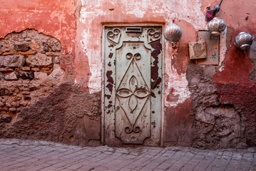 Green door in a red wall with silver lanterns on a street near the souk in Marrakesh, Morocco.