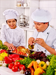 Happy middle-age man and young woman professional in chef hat cooking chicken.