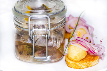 pickled herring in a glass jar with potato canapes