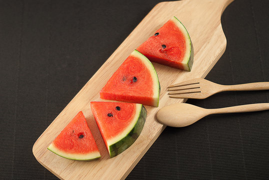 water melon slice on wood plate with fork and spoon isolated on black background