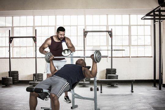 Trainer helping muscular man to lift the dumbell