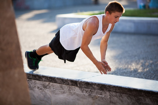 Teenager performing push-ups outdoor in city - Powered by Adobe