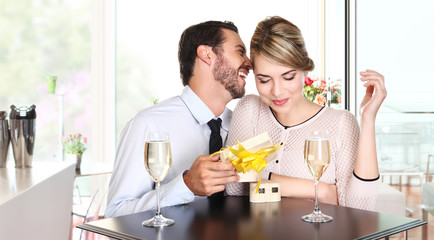 happy couple with gift sitting at a table with wine glasses