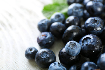 Tasty ripe blueberries with green leaves on wooden table close up