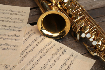 Beautiful golden saxophone with musical notes on wooden background, close up