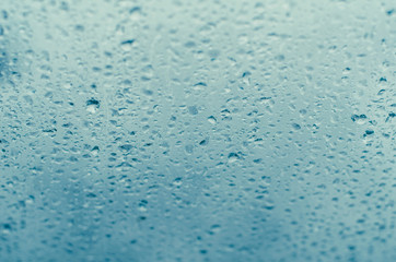 Droplets of rain on a window against a blue sky backdrop