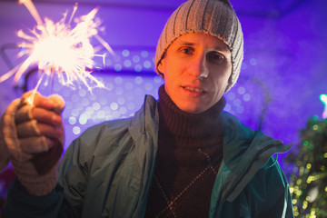 Man in winter clothes holding burning sparkler on New Year's Eve