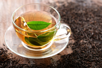 Glass cup of tea with green leaves on wooden background decorated with scattered tea
