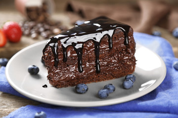 Chocolate cake with chocolate cream and fresh blueberries on plate, on wooden background