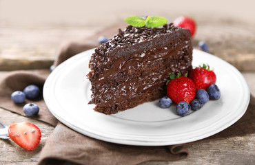 Chocolate cake with chocolate cream and fresh berries on plate, on wooden background