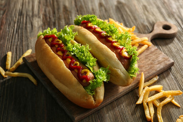 Delicious hot-dogs with French fries on wooden chopping board