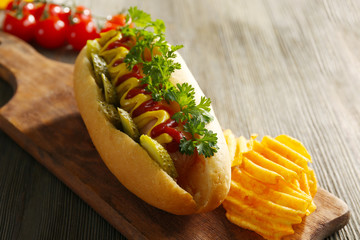 Delicious hot-dog with chips and vegetables on wooden background