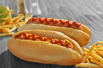 Delicious hot-dog with French fries and vegetables on wooden background