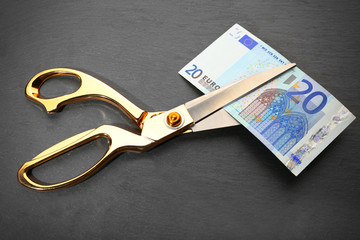 Golden scissors cut money on black background