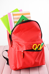 Red backpack full of stationery on wooden table against white background