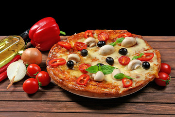 Delicious pizza and fresh vegetables on wooden table against black background, close up