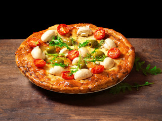 Tasty fresh pizza decorated with mushrooms and tomatoes on wooden table against black background, close up