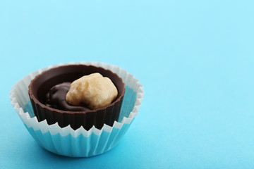 Chocolate candy with nut in paper cup, on blue background