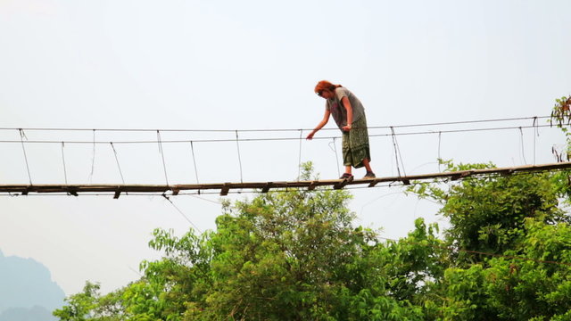 Tourist woman crossing dangerous bamboo suspension bridge, laos