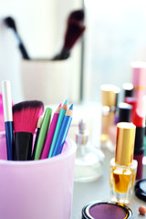 Makeup pencils, brush with cosmetics on a table, close up