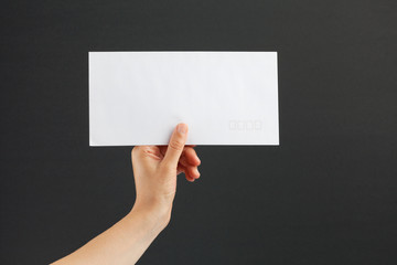 Female hand holding a white envelope on black background