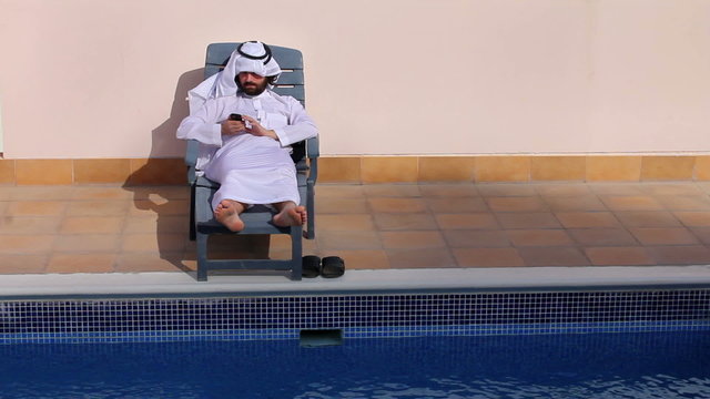 saudi arabian man using his phone at swimming pool