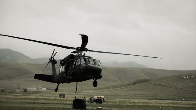 Shot from field of Black Hawk helicopter hauling off cargo.