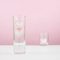 The lovely pink heart marshmallows in small narrow glass and shot glass on white table for Valentine's day.