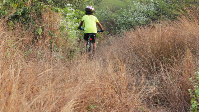 Teenage boy cycling downhill through thick and dry forest area