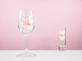 The lovely pink heart marshmallows in wine glass and small narrow glass on white table for Valentine's day.