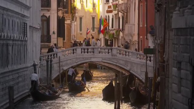 Gondoliers pass underneath a pedestrian bridge on a sunlit canal