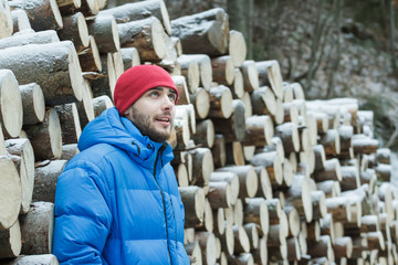 Resting woodcutter at wall of cut firewood background outdoors in winter mountain forest