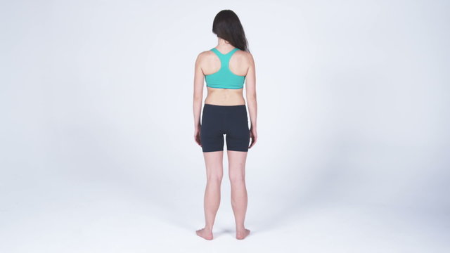 Back view of a woman in sports bra and gym shorts, putting hands on hips