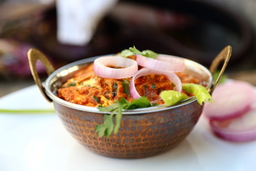 Butter chicken mutton curry or Indian style cottage cheese curry in a brass bowl with Salads.