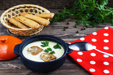 Cheese soup with croutons in pot on a wooden background