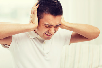 unhappy man closing his ears by hands at home