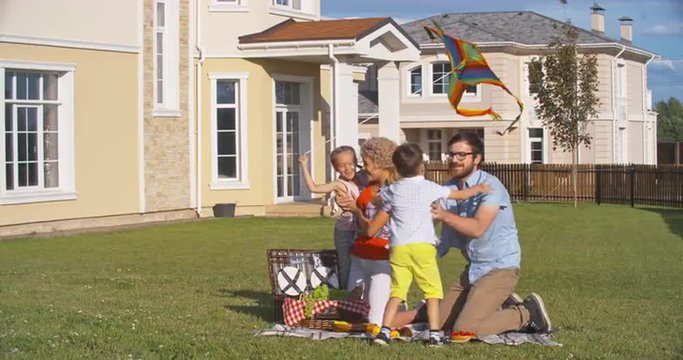 Young Family With Two Children Having Fun During Summer Picnic In Front Yard On Weekend 