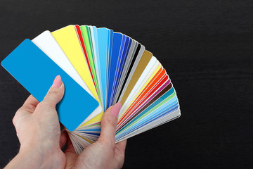 plastic color Swatch in the hands of a woman on a wooden black background
