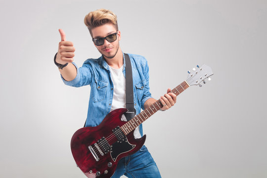 man in studio holding a guitar while showing the victory sign