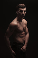 fit handsome man side posing in dark studio background while fle