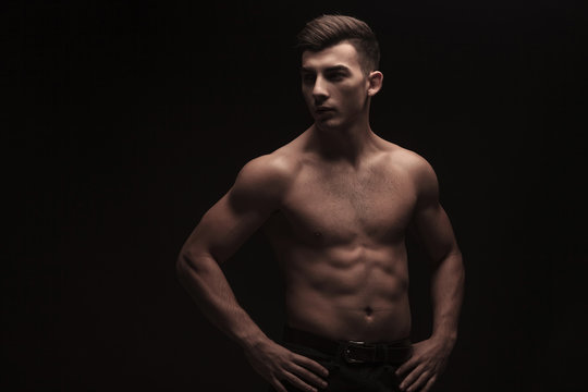fit young man posing in dark studio background with hands on wai
