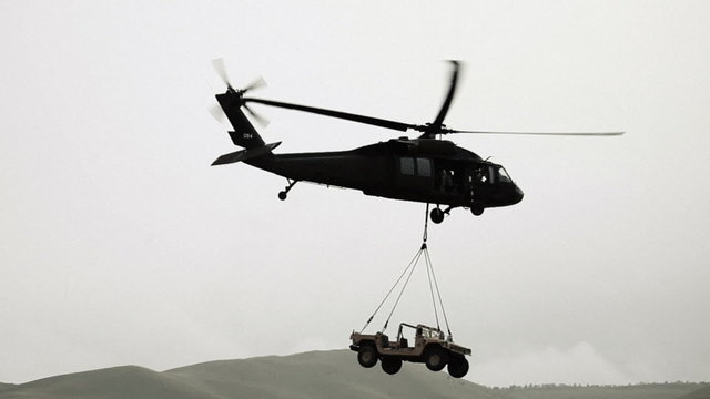 Humvee being hauled by Black Hawk helicopter from field.