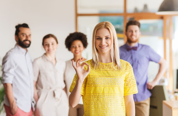 happy woman showing ok over creative office team