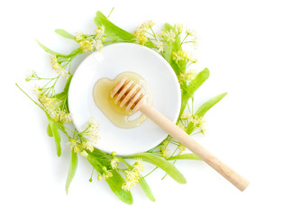 Honey dipper with honey with flowers of linden on white saucer, view from above