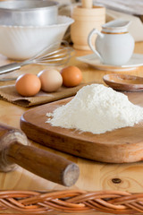 a bunch of white wheat flour, raw eggs, rolling pin, stainless steel whisk and other utensils on the kitchen table. close-up, selective focus. rustic style